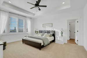 Carpeted bedroom with a raised ceiling and ceiling fan