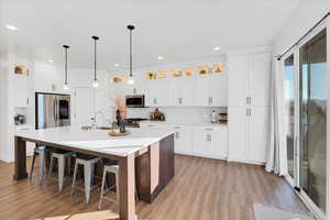 Kitchen with light wood-style flooring, an island with sink, white cabinets, appliances with stainless steel finishes, and tasteful backsplash