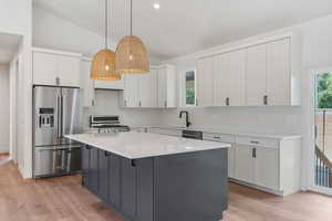 Kitchen with a center island, stainless steel appliances, vaulted ceiling, and white cabinets