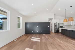 Kitchen with vaulted ceiling, white cabinets, decorative light fixtures, appliances with stainless steel finishes, and light hardwood / wood-style floors