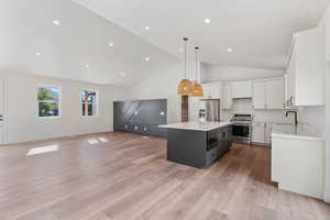 Kitchen featuring white cabinets, hanging light fixtures, a kitchen island, appliances with stainless steel finishes, and light wood-type flooring