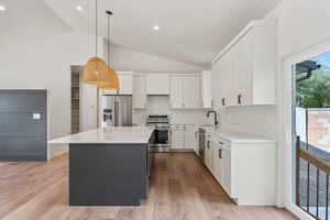 Kitchen featuring a kitchen island, white cabinetry, vaulted ceiling, pendant lighting, and stainless steel appliances