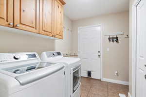 Clothes washing area with light tile patterned floors, cabinets, and separate washer and dryer