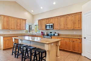 Kitchen featuring light stone countertops, appliances with stainless steel finishes, light tile patterned flooring, a kitchen bar, and a kitchen island