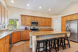 Kitchen with sink, appliances with stainless steel finishes, vaulted ceiling, and a kitchen island