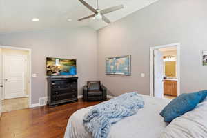 Bedroom with dark hardwood / wood-style flooring, high vaulted ceiling, connected bathroom, and ceiling fan