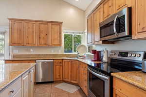 Kitchen with appliances with stainless steel finishes, light stone countertops, light tile patterned flooring, and sink