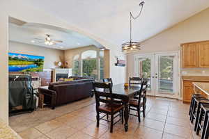 Tiled dining space featuring lofted ceiling, a wealth of natural light, and ceiling fan with notable chandelier