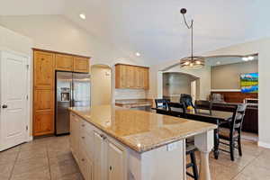 Kitchen featuring a large island, stainless steel refrigerator with ice dispenser, pendant lighting, and vaulted ceiling