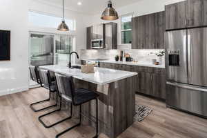 Kitchen with decorative backsplash, an island with sink, pendant lighting, and appliances with stainless steel finishes