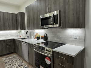 Kitchen with sink, dark brown cabinets, stainless steel appliances, tasteful backsplash, and light stone counters