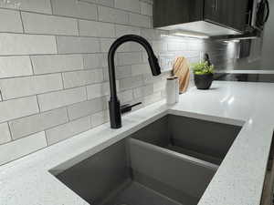 Room details with dark brown cabinetry, light stone countertops, sink, and backsplash