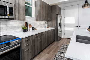 Kitchen with sink, decorative backsplash, light wood-type flooring, appliances with stainless steel finishes, and dark brown cabinetry