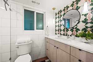 Bathroom featuring vanity, toilet, and tile walls