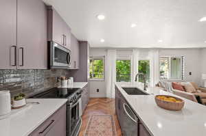 Kitchen featuring decorative backsplash, gray cabinetry, stainless steel appliances, sink, and light stone countertops