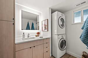 Clothes washing area with stacked washer / drying machine, sink, and dark hardwood / wood-style floors