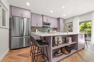 Kitchen featuring a kitchen breakfast bar, gray cabinetry, stainless steel appliances, backsplash, and sink