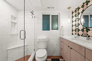 Bathroom featuring tile patterned floors, toilet, vanity, tile walls, and walk in shower