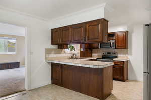 Kitchen with kitchen peninsula, decorative backsplash, appliances with stainless steel finishes, crown molding, and sink