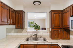 Kitchen with crown molding, decorative backsplash, sink, and tile countertops