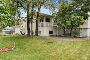 Rear view of property with a yard, a patio area, a hot tub, and a balcony