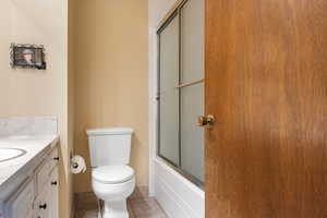 Full bathroom featuring vanity, shower / bath combination with glass door, toilet, and tile patterned flooring