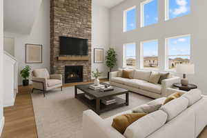 Living area featuring light wood-type flooring, baseboards, a towering ceiling, and a stone fireplace