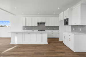 Kitchen featuring under cabinet range hood, white cabinetry, built in microwave, and light countertops