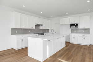Kitchen featuring light countertops, stainless steel microwave, stove, a sink, and wood finished floors