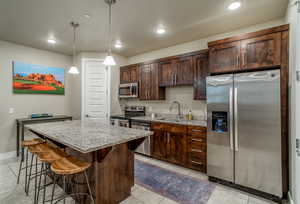 Kitchen with hanging light fixtures, appliances with stainless steel finishes, sink, dark brown cabinetry, and a center island