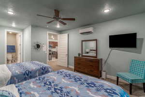 Carpeted bedroom featuring ceiling fan, a textured ceiling, ensuite bathroom, and a wall unit AC