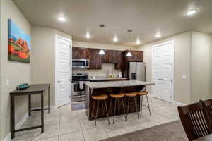 Kitchen featuring dark brown cabinets, a center island, stainless steel appliances, decorative light fixtures, and a breakfast bar