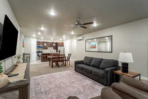 Living room with an AC wall unit, sink, light colored carpet, a textured ceiling, and ceiling fan