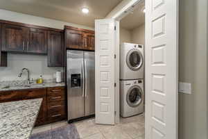 Laundry area with light tile patterned flooring, stacked washer / dryer, and sink