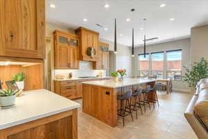 Kitchen with a breakfast bar area, a center island, light tile patterned flooring, decorative light fixtures, and tasteful backsplash