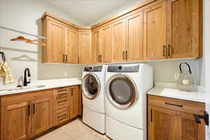 Washroom featuring light tile patterned floors, cabinets, sink, and washer and clothes dryer