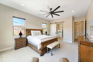 Bedroom with light colored carpet, ceiling fan, and a barn door