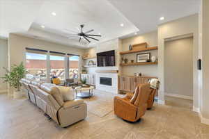 Living room featuring a tray ceiling, a fireplace, and ceiling fan