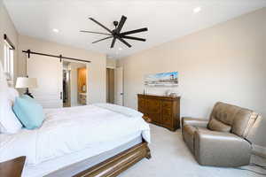 Bedroom with a walk in closet, ceiling fan, a barn door, a closet, and light colored carpet