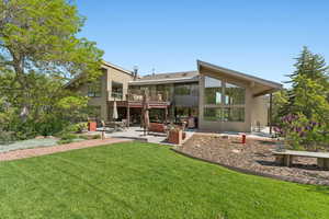 Rear view of house with a balcony, a patio area, stucco siding, and a yard