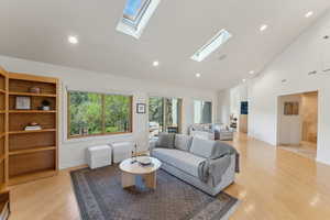 Living room with a skylight, high vaulted ceiling, light wood-style floors, recessed lighting, and baseboards