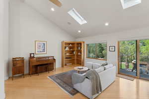 Living room featuring a skylight, light wood finished floors, recessed lighting, and high vaulted ceiling