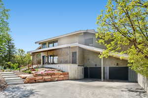 Contemporary home featuring driveway, stucco siding, stone siding, and stairway