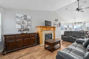 Living room with lofted ceiling, a tile fireplace, ceiling fan with notable chandelier, and light hardwood / wood-style floors