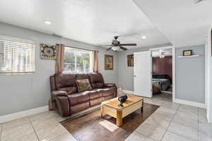 Living room with a textured ceiling, light tile patterned flooring, and ceiling fan