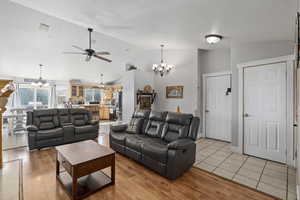 Living room featuring light hardwood / wood-style floors, a textured ceiling, vaulted ceiling, and ceiling fan with notable chandelier