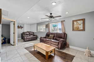 Living room featuring a textured ceiling, light tile patterned flooring, and ceiling fan