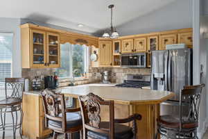 Kitchen with lofted ceiling, hanging light fixtures, backsplash, sink, and appliances with stainless steel finishes