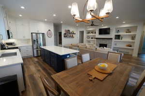 Dining room featuring a tiled fireplace, dark hardwood / wood-style floors, sink, built in shelves, and ceiling fan with notable chandelier