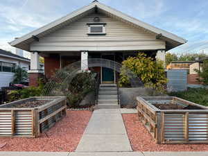 View of front of main house with covered porch, raised garden beds and xeriscape yard